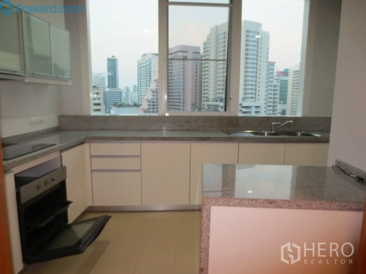 Condominium for rent in Khlong Toei, Bangkok - Bright U-shaped kitchen with granite countertops, built-in oven, double sink and skyline views through a large window.