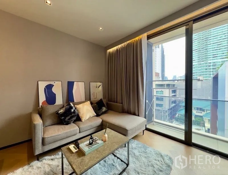 Condominium for rent or sale in Watthana, Bangkok - Bright living room with sofa, rug, and sliding glass doors to a balcony with city views.