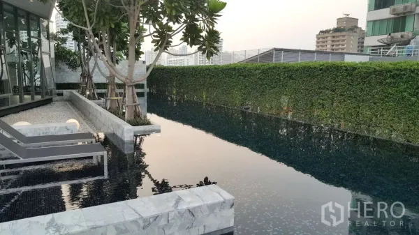 公寓 出租在Watthana, Bangkok - 公寓无边泳池，石材池畔、躺椅、绿篱与城市景观。