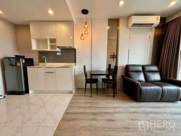 Condominium for rent or sale in Bang Na, Bangkok - Open-plan kitchen with glossy white cabinets, pendant lights and a dining set beside the living area.