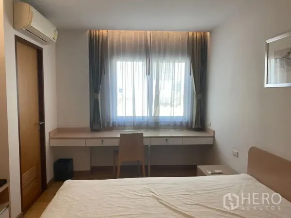 Condominium for rent or sale in Khlong Toei, Bangkok - Bedroom showing long built-in work desk under a large window with air conditioner above.