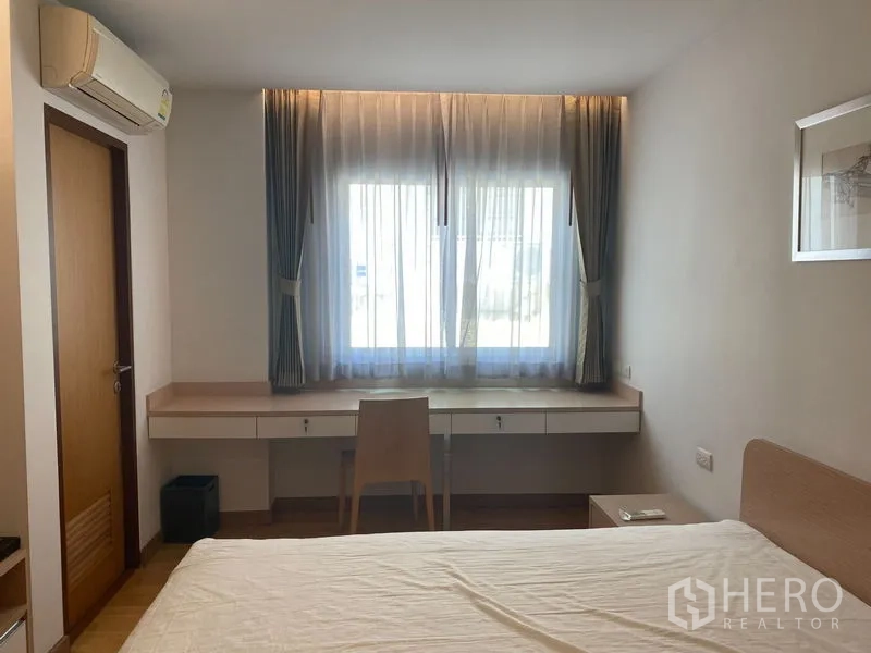 Condominium for rent or sale in Khlong Toei, Bangkok - Bedroom showing long built-in work desk under a large window with air conditioner above.