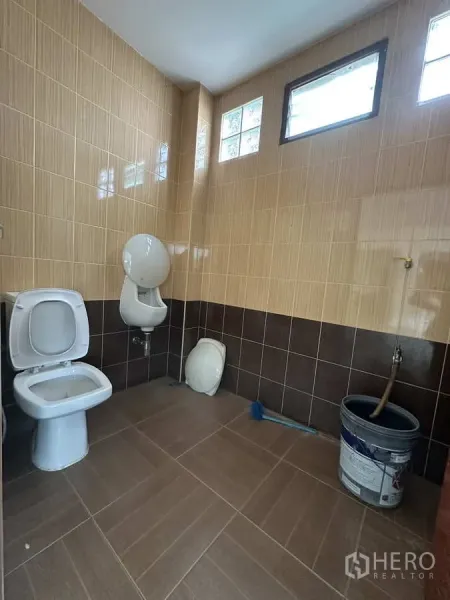 Factory for rent in Pathum Thani - Tiled restroom with toilet, urinal and high windows providing ventilation.