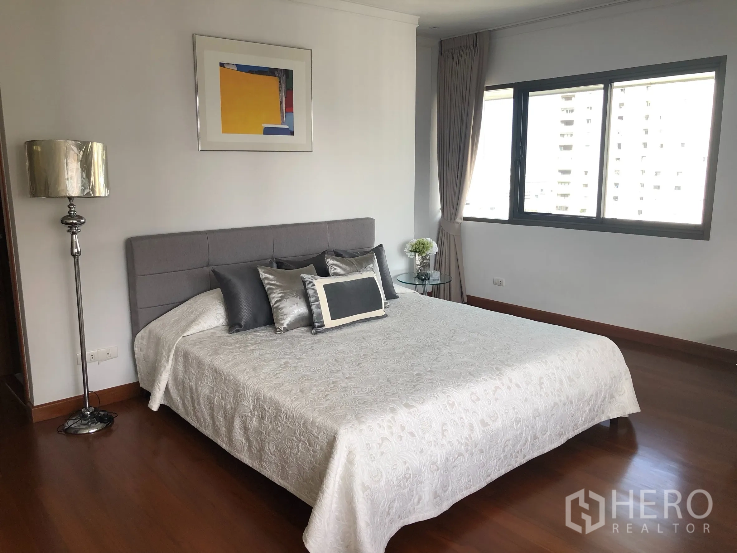 Condominium for rent in Bangkok - Master bedroom with grey upholstered headboard, large window and wood floors.