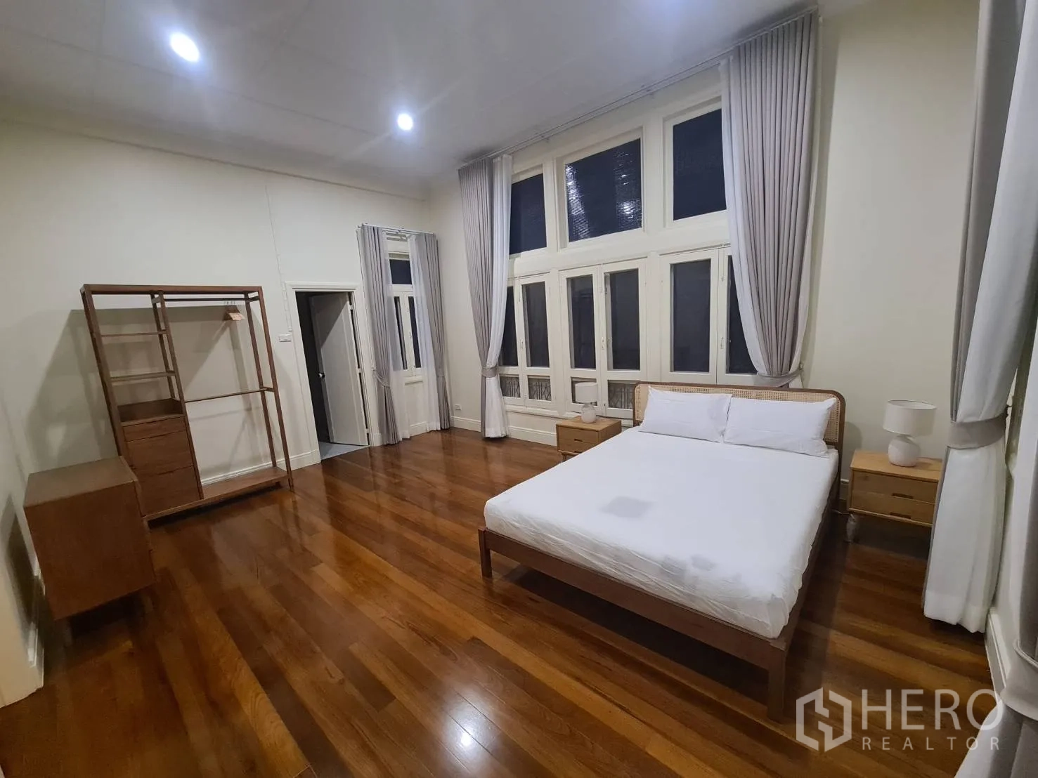 Detached House for rent in Khlong Toei, Bangkok - Bright bedroom with full-height windows, curtains and warm wood flooring.