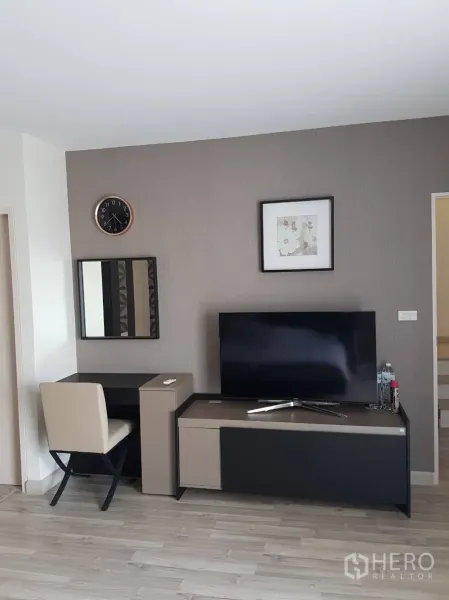Townhouse for rent or sale in Saphan Sung, Bangkok - Bedroom corner with TV stand, work desk, wall clock and neutral decor.