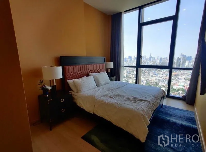 Condominium for rent in Watthana, Bangkok - Bedroom with large floor-to-ceiling window, bedside tables, and panoramic skyline view.