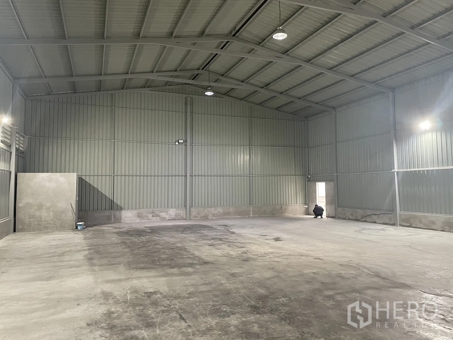 Factory for rent in Mueang Samut Prakan, Samut Prakan - Wide open warehouse interior with arched roof, concrete floor, wall lighting, and a service door.