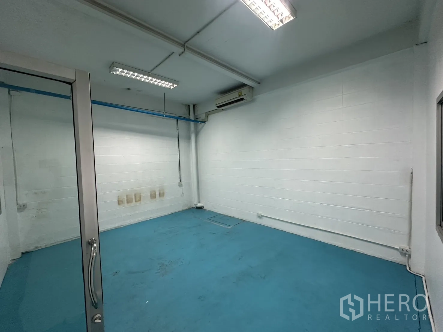 Warehouse for rent in Bang Na, Bangkok - Small air-conditioned office room with blue epoxy floor and glass door.