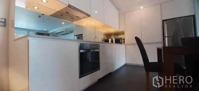 Condominium for rent in Phaya Thai, Bangkok - Sleek white kitchen with mirrored backsplash, under-cabinet lights and full-size appliances.