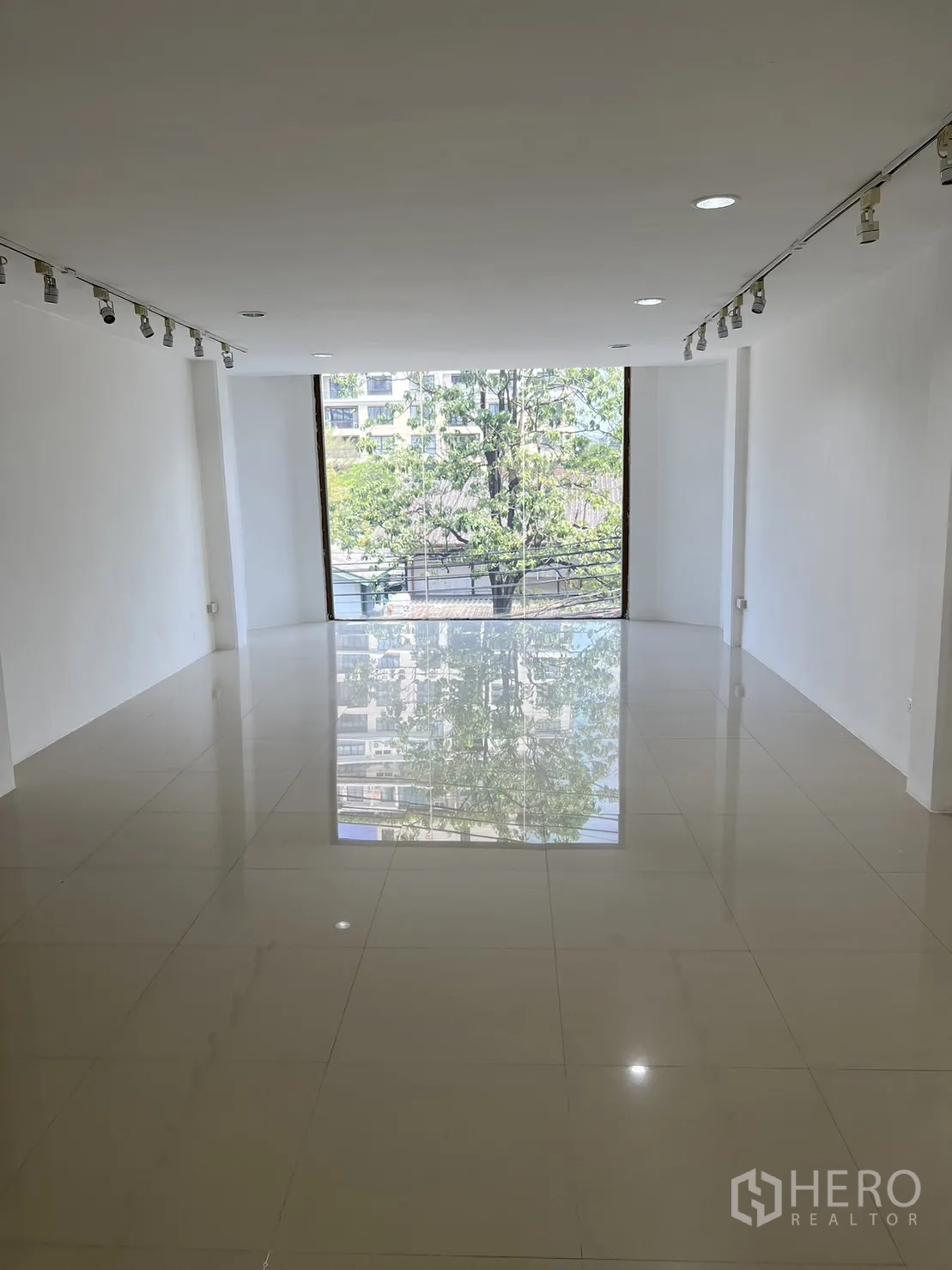 Shophouse for rent in Watthana, Bangkok - White showroom level with ceiling track lights and a floor-to-ceiling window.