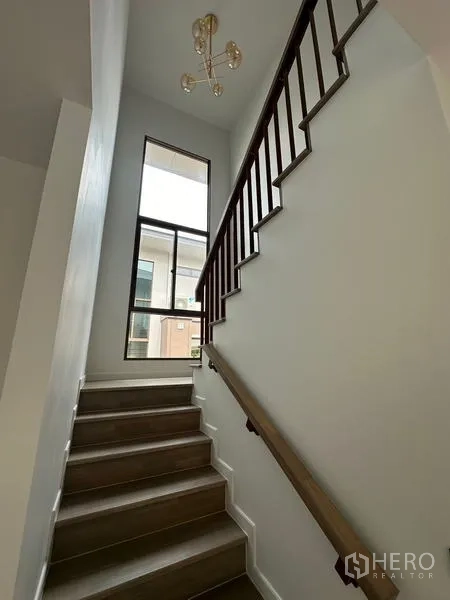 独立式住宅 出租在Bang Kapi, Bangkok - 楼梯配木质扶手与落地高窗，吊灯设计简洁现代。