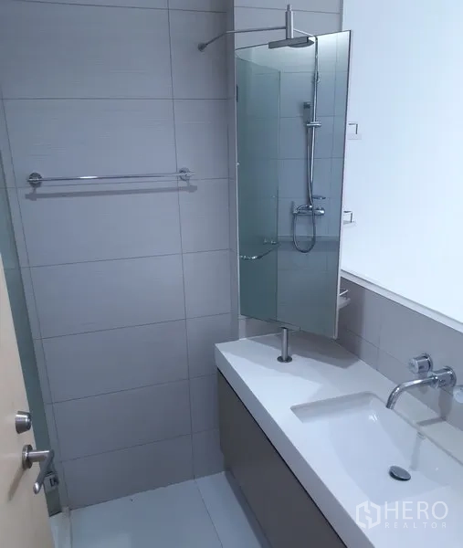 Condominium for rent in Khlong Toei, Bangkok - Contemporary bathroom with long vanity, wall‑mounted faucet, mirror, and glass shower.