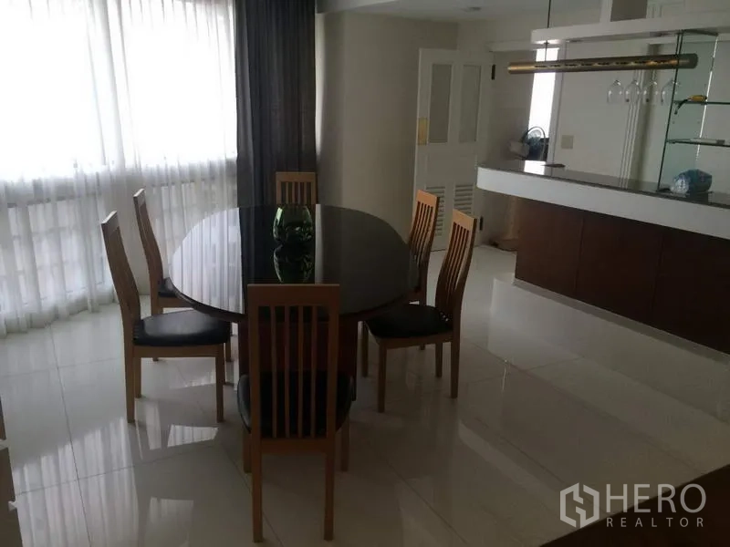 Condominium for rent in Khlong Toei, Bangkok - Dining area with round six-seat table, sheer floor-to-ceiling curtains and a bar counter at President Park condominium.