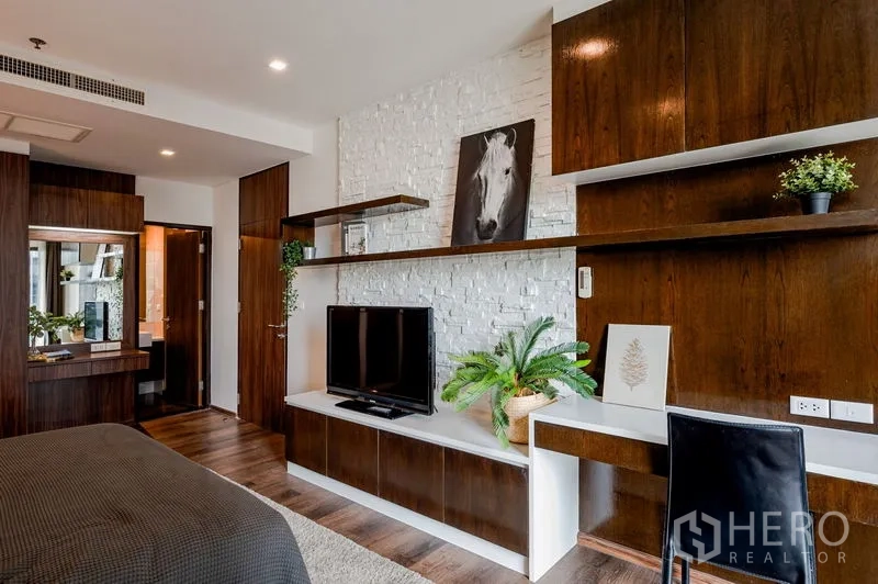 Condominium for sale in Khlong Toei, Bangkok - Bedroom media wall with TV, desk, dark wood cabinetry, and white brick accent.