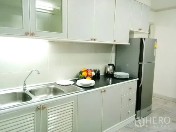 Condominium for rent in Watthana, Bangkok - Separate galley kitchen with white cabinets, double sink and stainless refrigerator.