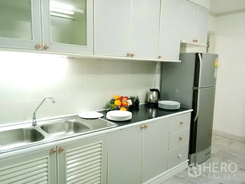 Condominium for rent in Watthana, Bangkok - Separate galley kitchen with white cabinets, double sink and stainless refrigerator.