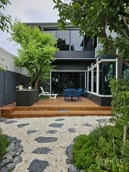 独立式住宅 出售在Thawi Watthana, Bangkok - 后部木质露台，户外餐桌与玻璃阳光房。
