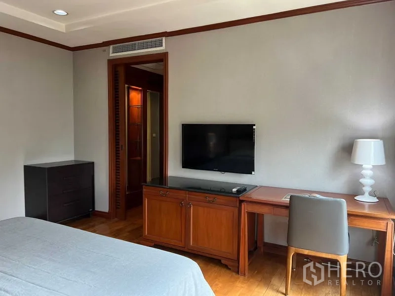 公寓 出租或出售在Phra Khanong, Bangkok - 卧室一角，壁挂电视、木质书桌与通往卫浴的门。