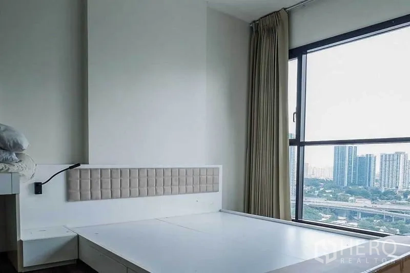 Condominium for rent in Khlong Toei, Bangkok - Master bedroom with platform bed base and floor-to-ceiling window offering a city view.