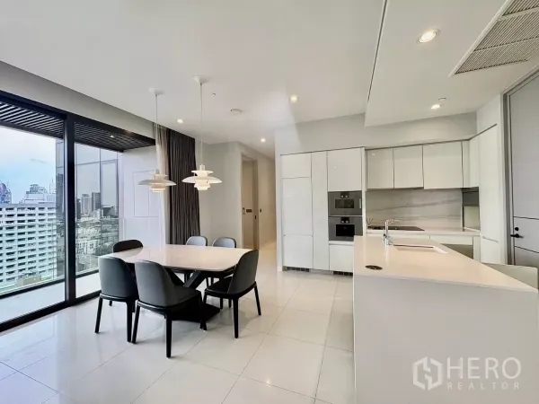 公寓 出租在Watthana, Bangkok - 六人餐桌，旁为白色嵌入式厨房与中岛，可眺望城市。