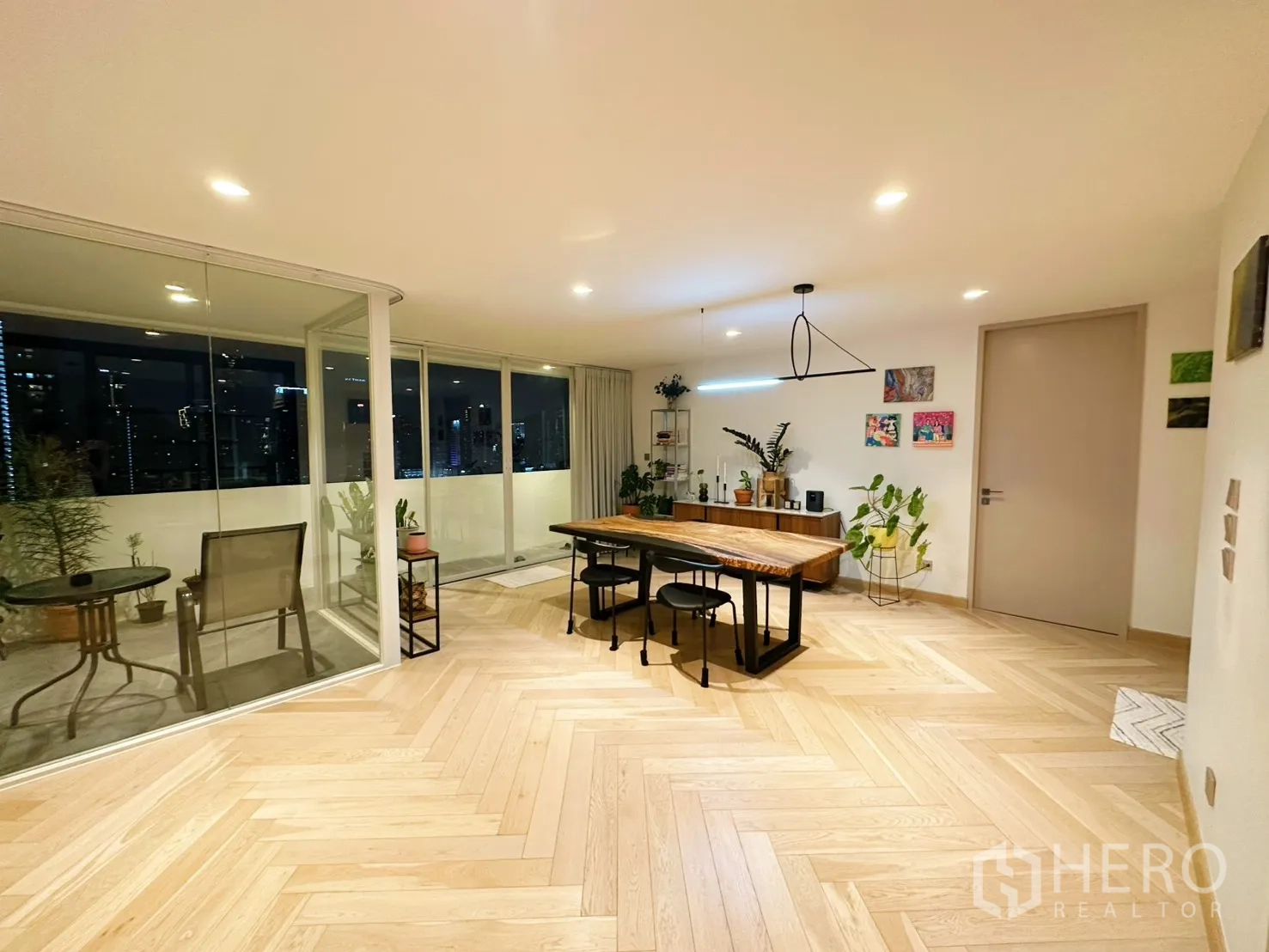 Condominium for rent or sale in Watthana, Bangkok - Dining space with statement light beside a wide balcony and indoor plants at night.