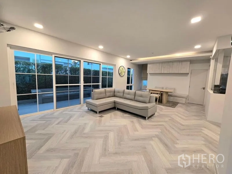 Detached House for rent in Bang Phli, Samut Prakan - Open‑plan living room with L‑shaped sofa, sliding glass doors and herringbone floors.