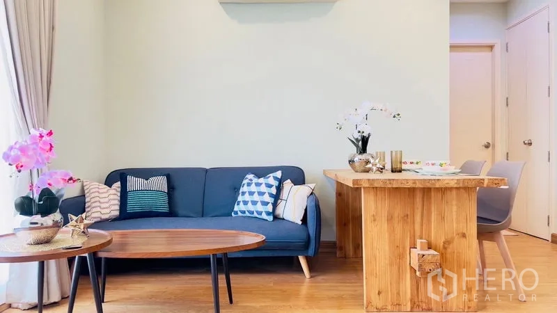 Condominium for rent in Watthana, Bangkok - Living room with blue sofa, wooden coffee tables, orchids and dining counter.