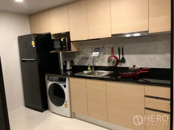 公寓 出租或出售在Yan Nawa, Bangkok - 一字型整体厨房，浅木柜体、黑色台面，配冰箱、微波炉和洗衣机。