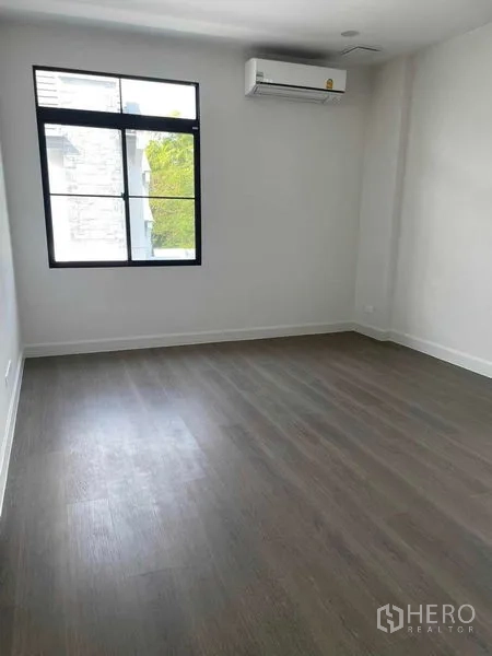 Detached House for sale in Saphan Sung, Bangkok - Spacious bedroom with wood flooring, air conditioner, and greenery view.