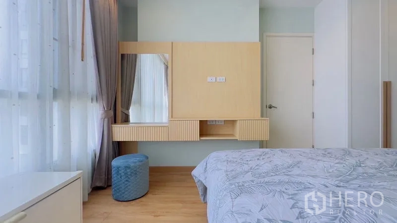 Condominium for rent in Watthana, Bangkok - Bedroom vanity with wall mirror, built-in wooden desk and blue ottoman.