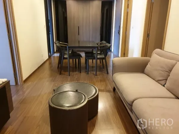 公寓 出租在Watthana, Bangkok - 温馨客厅，米色沙发、叠放茶几与餐桌，木地板。