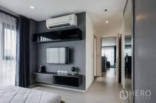 Condominium for rent in Khlong Toei, Bangkok - Bright bedroom with wall-mounted TV, floating console, and air conditioning beside a window with sheer curtains.