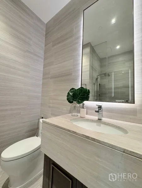 Condominium for rent in Watthana, Bangkok - Modern bathroom with backlit mirror, stone vanity, toilet and glass shower enclosure.