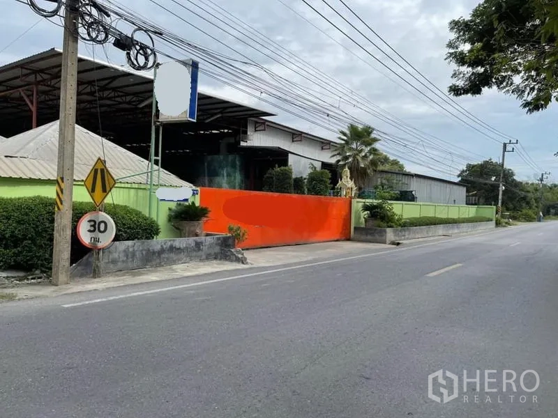 คลังสินค้า ขายในLam Luk Ka, Pathum Thani - มุมมองด้านหน้าโกดัง เห็นประตูบานเลื่อนสีส้ม ป้ายริมทาง และกันสาดโครงเหล็กกว้าง