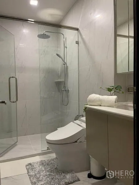 Condominium for rent in Ratchathewi, Bangkok - Modern bathroom with marble tiles, glass shower enclosure and rain shower.