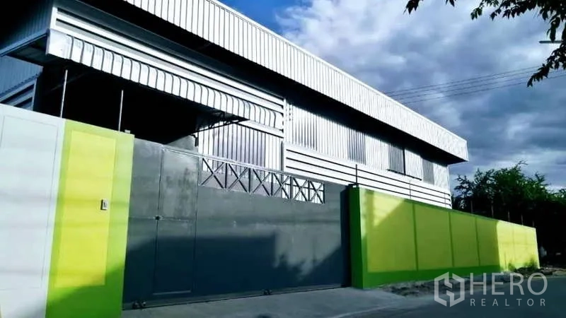 Warehouse for rent in Mueang Samut Sakhon, Samut Sakhon - Street view of corrugated metal warehouse facade with large sliding gate and bright green wall.