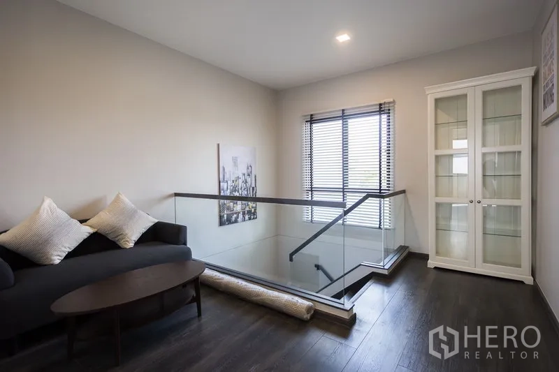 Townhouse for rent in Samut Prakan - Upper landing lounge with glass balustrade, sofa and display cabinet.