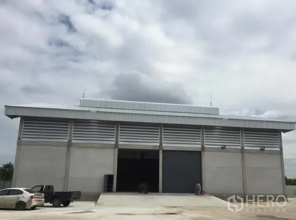 Warehouse for rent in Khlong Sam Wa, Bangkok - Front view of the warehouse showing twin roller shutter doors, wide driveway, and concrete parking apron.