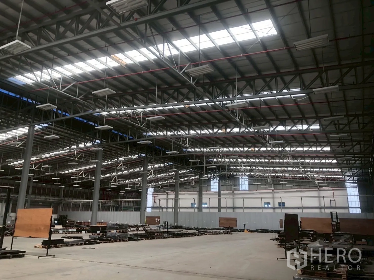 Factory for rent in Pluak Daeng, Rayong - Warehouse interior showing trusses, lighting, and materials arranged on pallets.