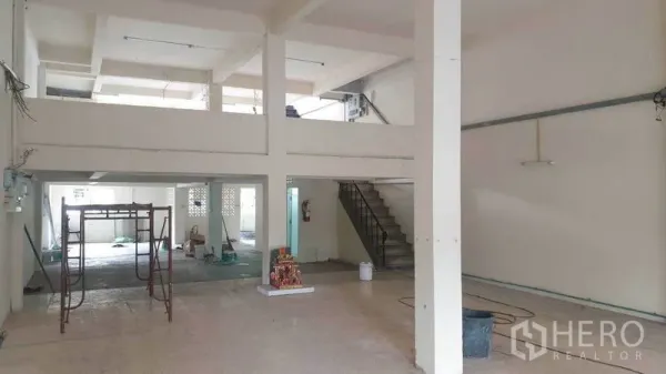 Shophouse for rent in Phra Khanong, Bangkok - Open-plan hall with high ceiling, mezzanine and stairs, with light renovation underway.