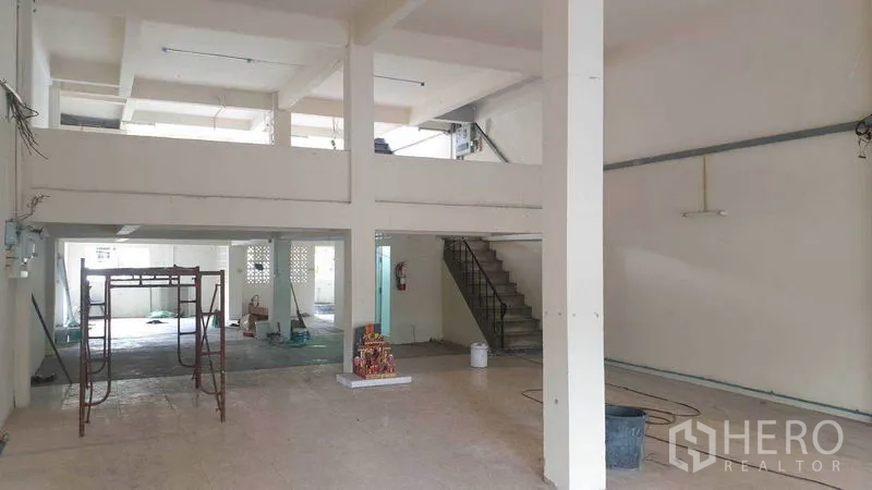 Shophouse for rent in Phra Khanong, Bangkok - Open-plan hall with high ceiling, mezzanine and stairs, with light renovation underway.