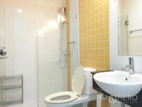 Condominium for rent in Khlong Toei, Bangkok - Modern bathroom with walk-in glass shower, yellow feature tiles and vanity sink.