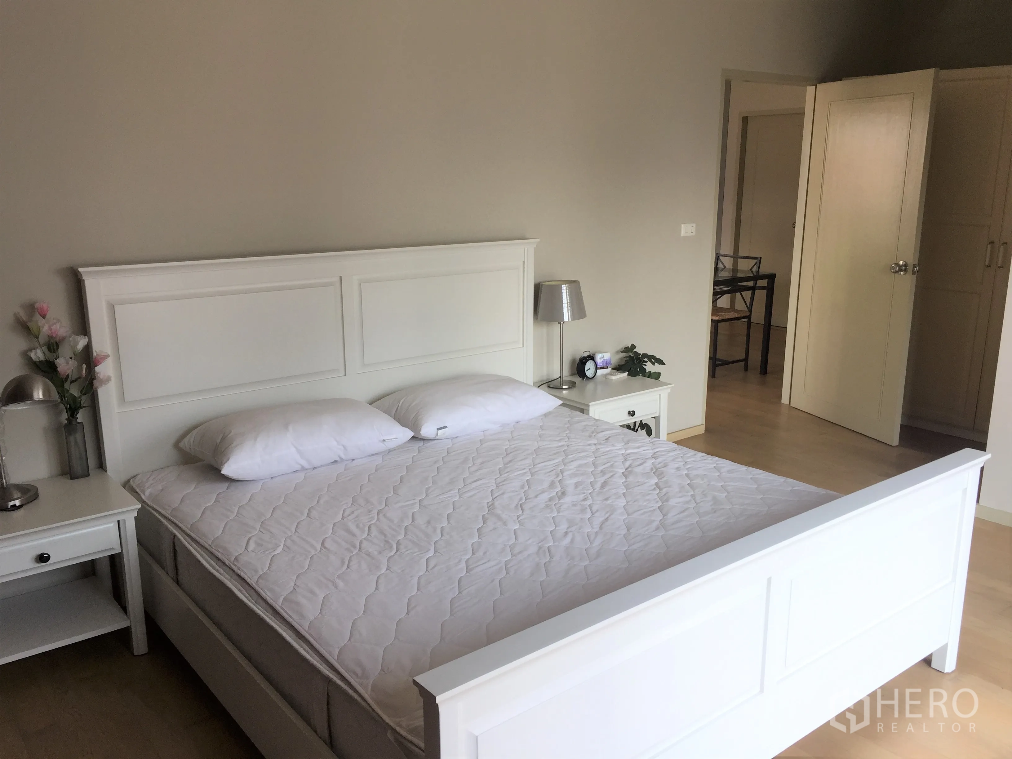 Condominium for rent or sale in Watthana, Bangkok - Spacious master bedroom with white bedframe, bedside tables and hardwood flooring.