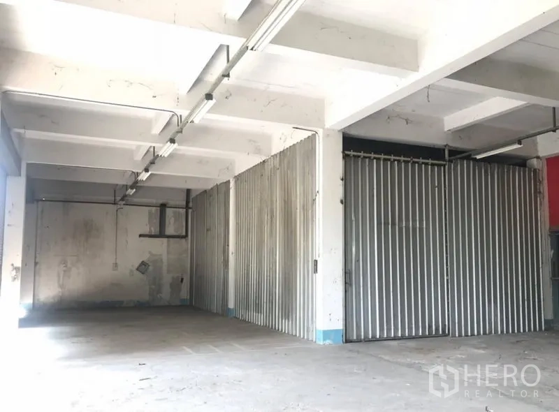 Warehouse for rent in Bueng Kum, Bangkok - Storage bays with metal sliding doors and long fluorescent lighting beneath a concrete beam ceiling inside the warehouse.