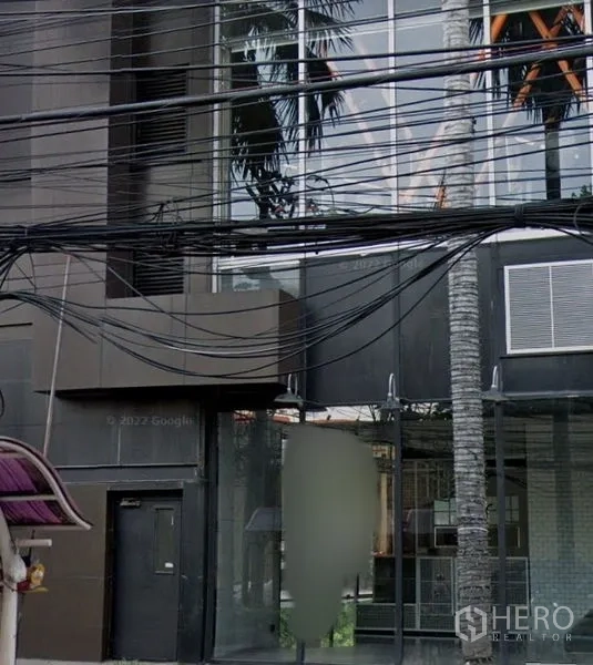 พื้นที่ขายปลีก ให้เช่าในWatthana, Bangkok - มุมมองระดับถนนของอาคารพาณิชย์หน้ากระจกสีเข้ม กระจกสูงจรดเพดาน มีต้นปาล์มและสายไฟเหนือศีรษะ