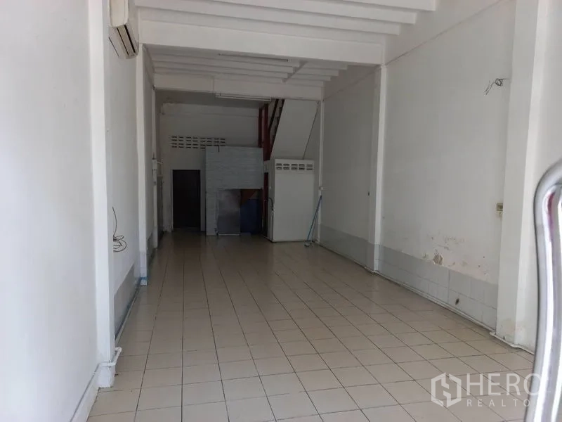 Shophouse for rent in Khlong Toei, Bangkok - Open-plan ground floor of a shophouse with white walls, tiled flooring, high ceiling beams and a rear service area with bathroom door.