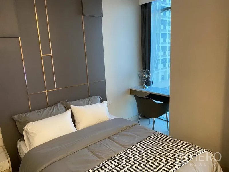 Condominium for rent in Khlong Toei, Bangkok - Cozy bedroom with padded feature wall, bed linens and desk by the window with city outlook.