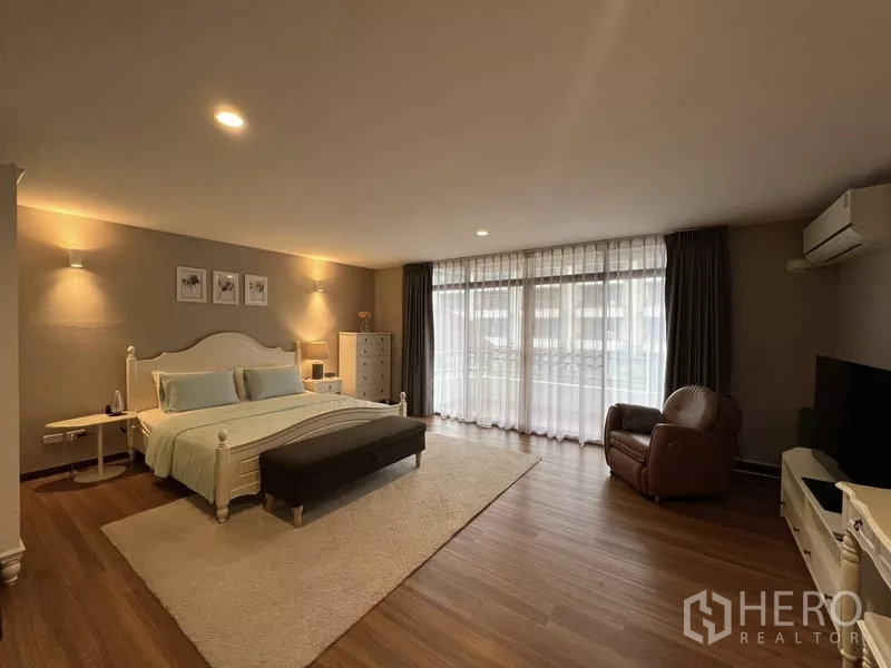 Townhouse for rent or sale in Suan Luang, Bangkok - Master bedroom with armchair, TV and doors to the balcony.