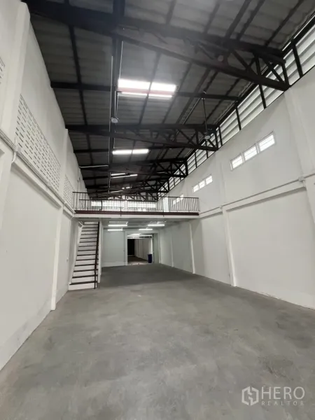Shophouse for rent in Khlong Toei, Bangkok - Double-height shophouse hall with mezzanine, steel trusses and concrete floor.